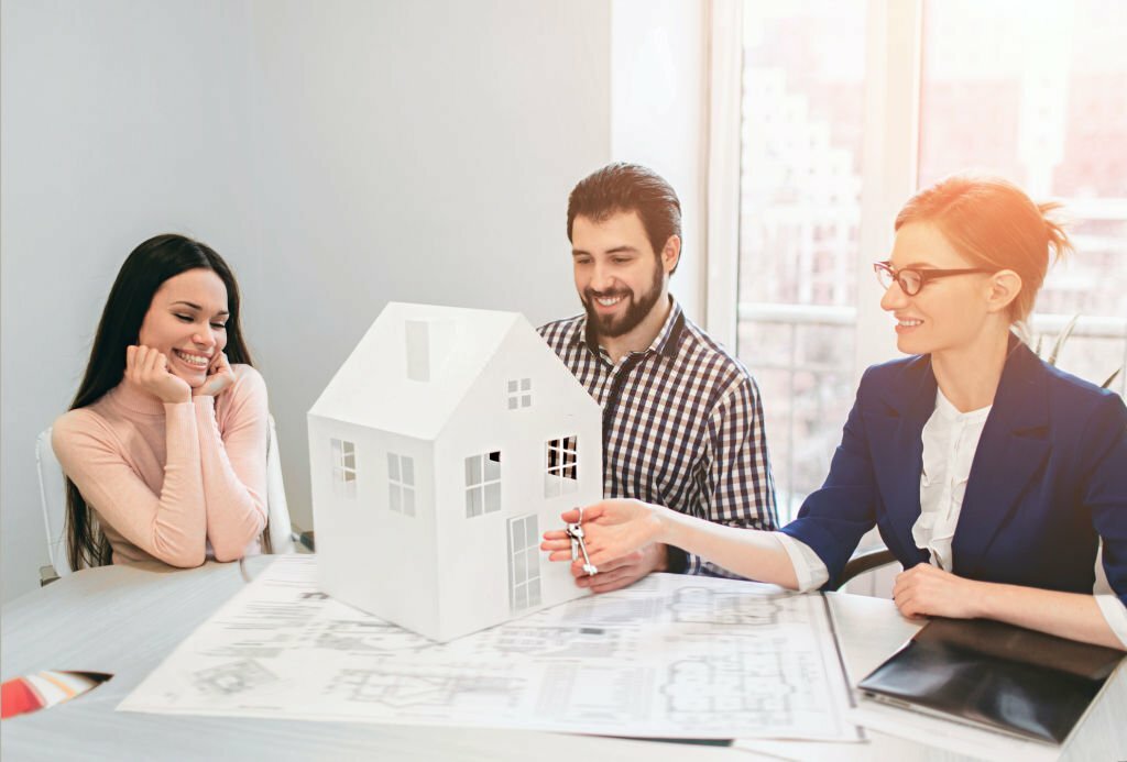Young family couple purchase rent property real estate . Agent giving consultation to man and woman. Signing contract for buying house or flat or apartments. He holds a model of the house in hands.